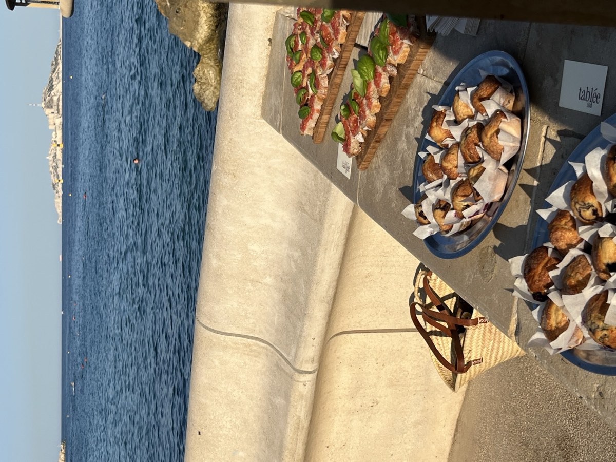 Buffet de tablée sud dressé sur un muret en bord de mer à Marseille : tartines tomate-basilic et plateaux de muffins face aux îles